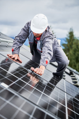 Man roofer mounting photovoltaic solar panels on roof of house. Engineer in helmet installing solar module system with help of hex key. Concept of alternative, renewable energy.の写真素材