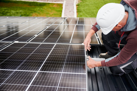 Man technician mounting photovoltaic solar panels on roof of house. Engineer in helmet installing...