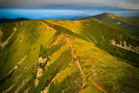 Breathtaking aerial view of green, rugged mountain peaks under dramatic sky. Scene captures contrast...