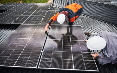 Professional technicians adjusting solar PV panels. Solar system installation on roof of house. Top view of two male workers in halmets and work overalls securing solar battery.の写真素材
