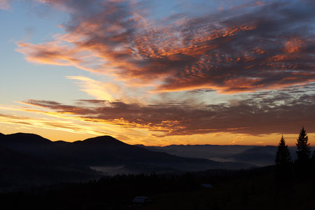 Breathtaking sunset paints sky with vibrant hues of pink, orange, purple, blending into blue morning sky. Silhouetted mountains, pine trees create serene backdrop. Tranquil and picturesque landscape.の写真素材