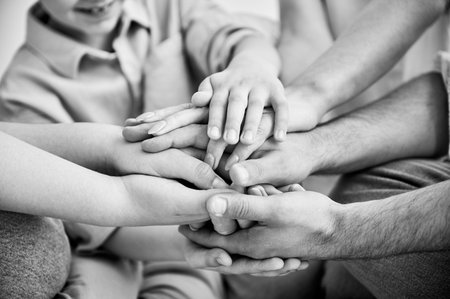 Close-up of several hands placed on top of one another in stack. Big family putting stacked hands together promising work in team. All family members showing support to each other. Black and white.の写真素材