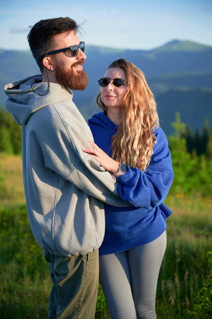 Portrait of couple stand close together in scenic meadow with mountains in background. Man and woman...