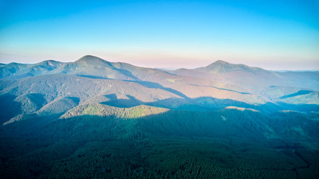 Breathtaking aerial view of mountain landscape at sunset. Golden light bathes rolling hills and lush forests, creating serene and idyllic scene. Distant mountains adding depth to picturesque vista.の写真素材