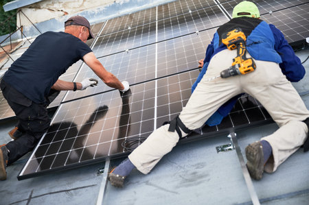 Workers building solar panel system on metal rooftop of house. Two men installers installing...