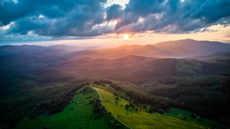 Aerial view breathtaking sunset over forest. Suns rays break through dramatic clouds, casting golden...