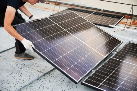 Worker building solar panel system on metal rooftop of house. Man engineer installing photovoltaic solar module outdoors. Alternative, green and renewable energy generation concept.の写真素材