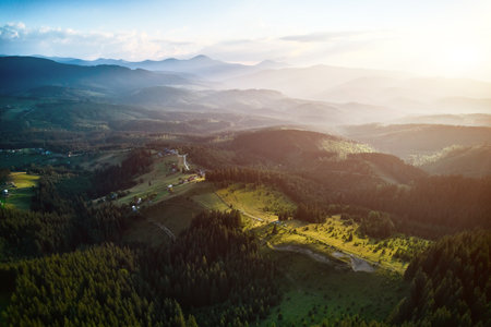 Breathtaking aerial view of mountain landscape at sunset. Golden light bathes rolling hills and lush...