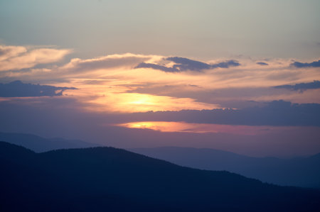 Clouds in sky at evening above hills. Beautiful view of landscape in mountains, sun sitting in...