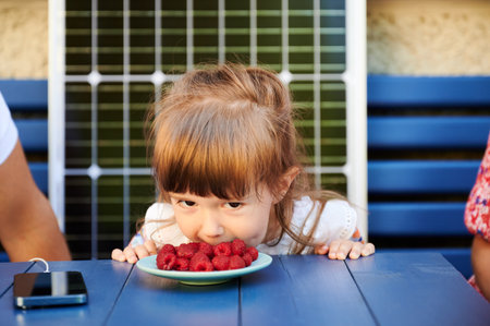 Lovely moment of child eating berries without hands. Daughter having fun with her parents. Little...
