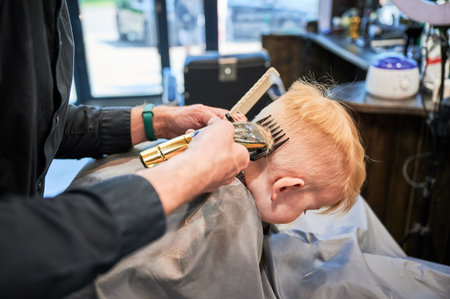 Little boy getting his first haircut. Back view of hairdresser shaving head. Cute client in barbershop.の写真素材