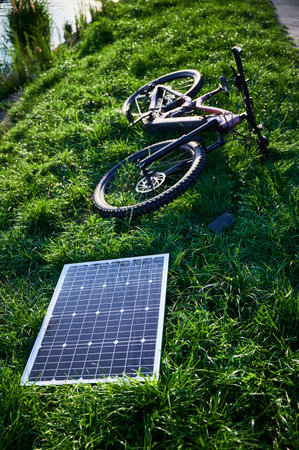 Pink electric mountain bike lies on lush green grass, connected to solar panel for charging. Bicycle beside paved path, showcasing bikes rugged tires and sleek design in outdoor environment.の写真素材