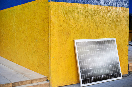 Solar panel against vibrant wall painted in blue and yellow colors of Ukrainian flag. Scene symbolizes integration of sustainable renewable energy solutions within culturally significant context.の写真素材