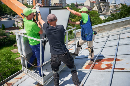 Workers lifting up photovoltaic solar panel on metal rooftop of house with assistance of crane lift....