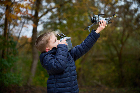A boy enthusiastically operates a drone amid vibrant fall foliage. The cool air adds to the excitement as he captures the beauty around him with his device.の写真素材
