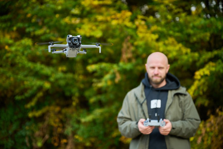 A man control a sleek drone in a lush area filled with colorful autumn trees, showcasing his skills...