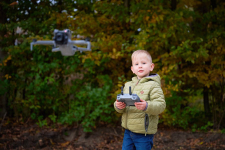 A young boy operates a drone with enthusiasm in a vibrant park filled with colorful autumn leaves....