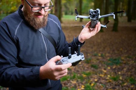 A man enjoys flying a drone in a vibrant green forest. He carefully checks the remote control as sunlight filters through the trees, creating a serene atmosphere.の写真素材