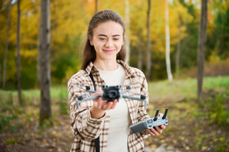A person is enjoying outdoor drone flying in a colorful forest. They are smiling while holding the...