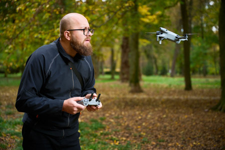 In a serene forest filled with golden autumn leaves, a man skillfully controls his drone, enjoying...