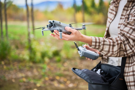 A person holds a sleek drone ready for flight among vibrant trees in a picturesque outdoor...
