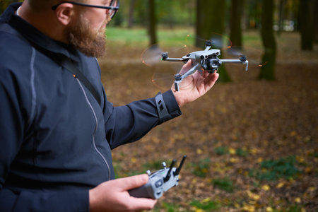 A man stands in a peaceful forest, holding a drone in one hand and a remote control in the other.