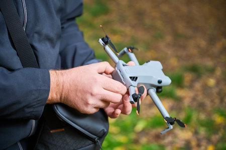 A person adjusts a drone in a lush forest filled with colorful autumn leaves on a calm afternoon....