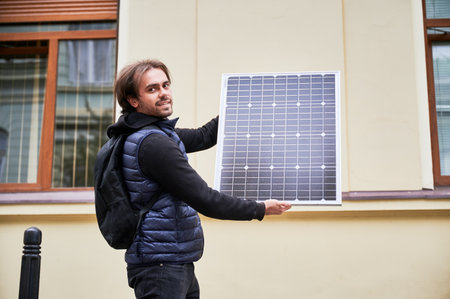 Man holding photovoltaic solar panel in front of historical building. Concept of integration of...