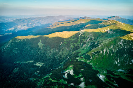 Aerial view of rugged mountain range with lush green slopes at sunset. Landscape showcases beauty of untouched nature with distant peaks and valleys bathed in soft sunlight. Carpathians, Chornogora.の写真素材