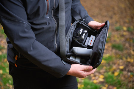 A person holds an organized bag filled with outdoor gear while surrounded by colorful autumn leaves,...