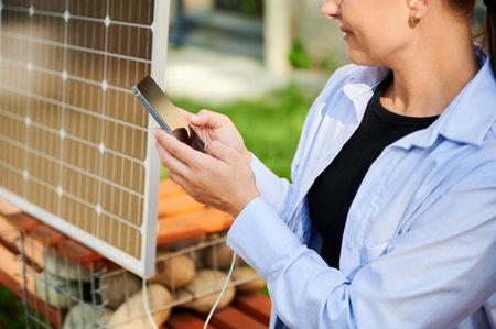 Happy woman using smartphone connected to solar panel. Cropped view. Integration of sustainable renewable energy into everyday life, demonstrating practical use of solar power for charging devices.の写真素材