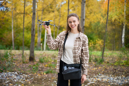 A young woman stands in vibrant forest, holding a drone with excitement. Surrounded by golden...