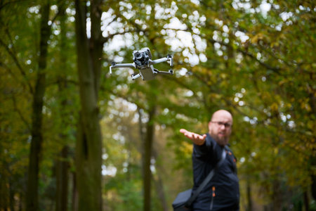 In a lush forest during autumn, a man extends his hand as a drone takes flight, exploring the rich...