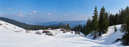 Serene winter scene with small alpine village blanketed in snow. Rustic cabins dot snowy landscape,...