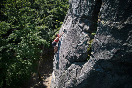 Aerial view of woman rock climber ascending rugged limestone cliff with harness and rope for safety....