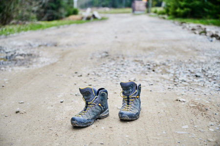 Close up of worn hiking boots on dirt road, abandoned trekking footwear on trail, outdoor adventure concept with shallow depth of field