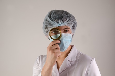 Doctor with magnifying glass. Confident middle-aged male doctor holding a magnifying glass in front of his eyeの写真素材