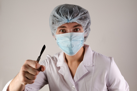 portrait of doctor in mask and hat keep scalpel on neutral background.の写真素材
