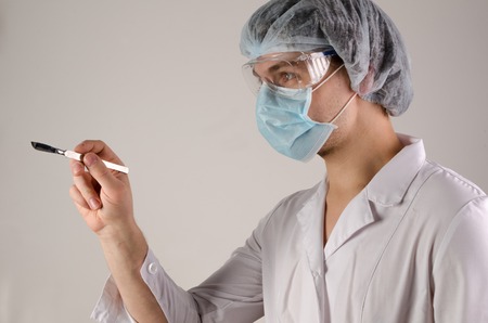 portrait of doctor in mask and hat keep scalpel on neutral background.の写真素材