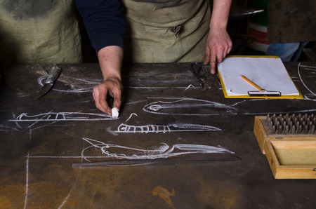 Table in a forge. Planning design of knife. Craftsman stands near the tableの写真素材