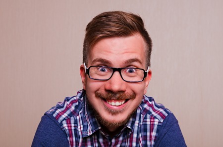 young man in dark glasses, red shirt in blue cage smiling. Happy smiling man with wide open mouth and eyes. European brunette feels joyの写真素材