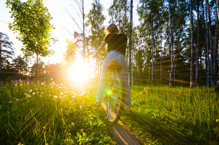 Woman in black shirt and blue jeans ride by bycicle outdoor in the park.の写真素材