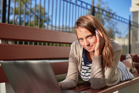 Freelance. Girl making job outdoor on the bench. Portrait of happy woman. Using wireless technology for internet surfing. Working with laptop in the street.の写真素材