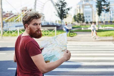 Tourist explore new city. Hansome man with big beard in red t shirt walk in the city to learn more about it. Guy stay in font of crosswalk and look backの写真素材
