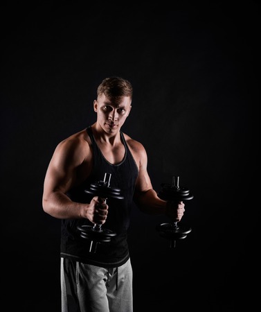 Fitness trainer with dumbbells on black background. Man making training exercises. Concept of healthy life. Strong person look to the camera.の写真素材