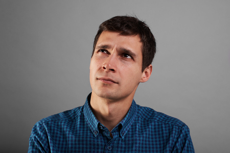 Thinking man on neutral background. Europian dreaming face search new idea. Studio portrait of handsome guy. Male in blue shirt.の写真素材