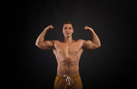 Front view on trained bodybuilder torso. Man show biceps. Portrait of pumped up man on black background. Relief body concept.の写真素材