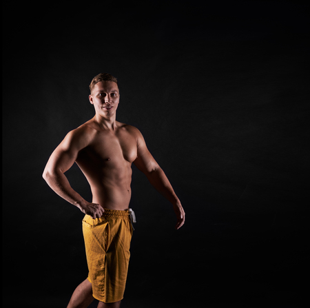Bodyduilder pose. Dark concept of fitness man. Sport life results. Strong person posing and look to the cameraの写真素材