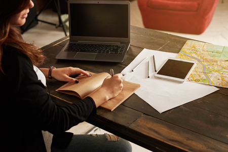 Mockup with wood table, notebook, tablet, city map, white sheets in modern loft. Woman write notes about new startup. Free space for a advertising product.の写真素材