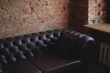 Modern loft interior with red brick wall, leather sofa, wooden windowsill. Copy space for your advertising text. Day time with street natural light.の写真素材